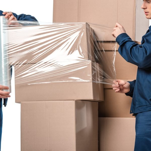 two movers wrapping cardboard boxes with roll of stretch film isolated on white